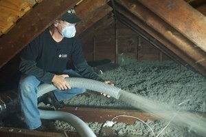 A man wearing a mask applies insulation in an attic.