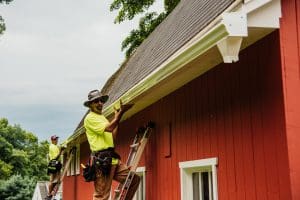 Two workers installing seamless gutters on a red house.
