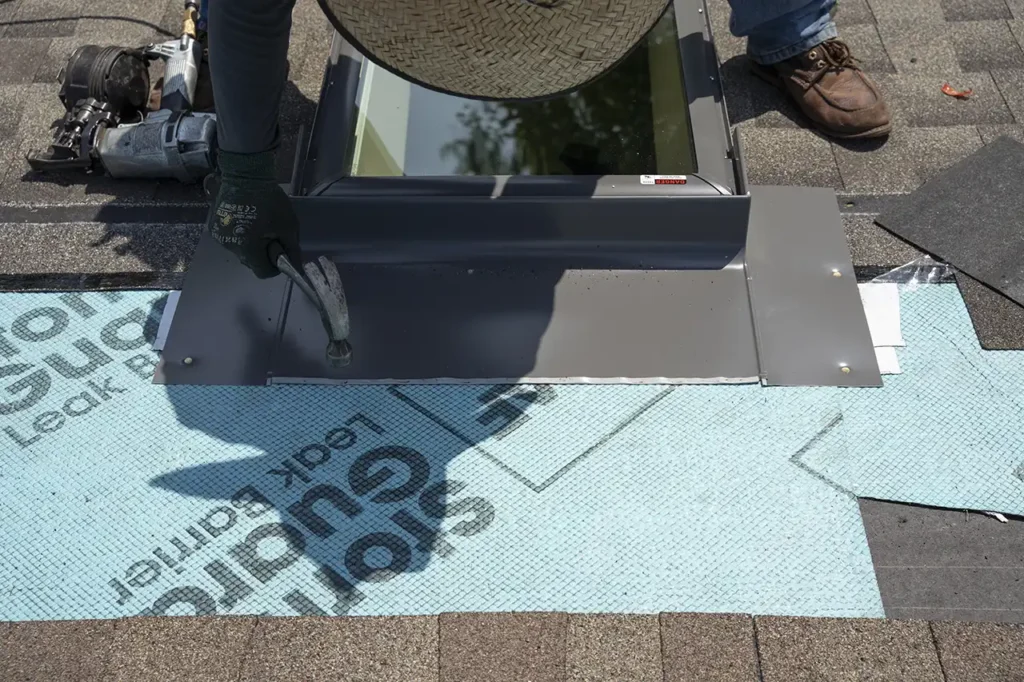 Roofing contractor installing metal flashing around a skylight on an asphalt shingle roof